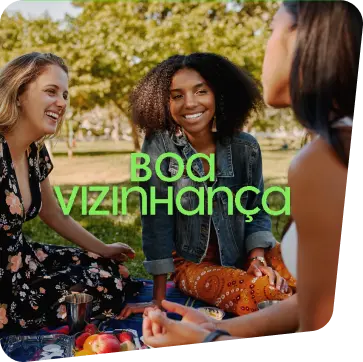 Três mulheres sentadas em uma roda de piquenique em uma área verde conversando e sorrindo.