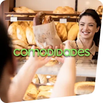 Duas mulheres em uma padaria, sendo uma atendente entregando a sacola de pães para a sua cliente que está do outro lado do balcão.